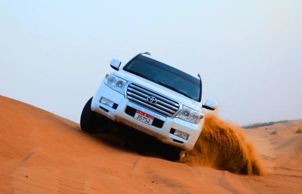 White SUV performing dune bashing in the Abu Dhabi desert, kicking up sand.